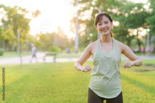 Fototapeta Naklejka Na Ścianę i Meble -  Female jogger. Fit young Asian woman with green sportswear stretching muscle in park before running and enjoying a healthy outdoor. Fitness runner girl in public park. Wellness being concept