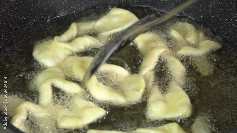 Chef stirs the biscuits in the boiling oil with a metal kitchen spatula. Cooking deep-fried dough. Fatty cooking Chef stirs the biscuits in the boiling oil with a metal kitchen spatula. Cooking deep-fried dough. Fatty cooking