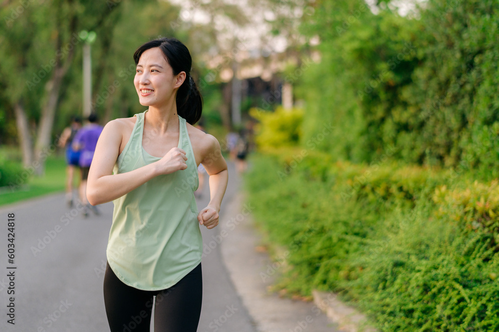 Fit Asian young woman jogging in park smiling happy running and enjoying a healthy outdoor lifestyle. Female jogger. Fitness runner girl in public park. healthy lifestyle and wellness being concept Fit Asian young woman jogging in park smiling happy running and enjoying a healthy outdoor lifestyle. Female jogger. Fitness runner girl in public park. healthy lifestyle and wellness being concept
