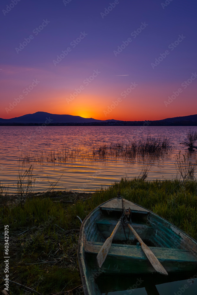 Malowniczy zachód słońca nad jeziorem ze starą łodzią z wiosłami i bezchmurnym niebem w tle, Polska - obrazy, fototapety, plakaty 