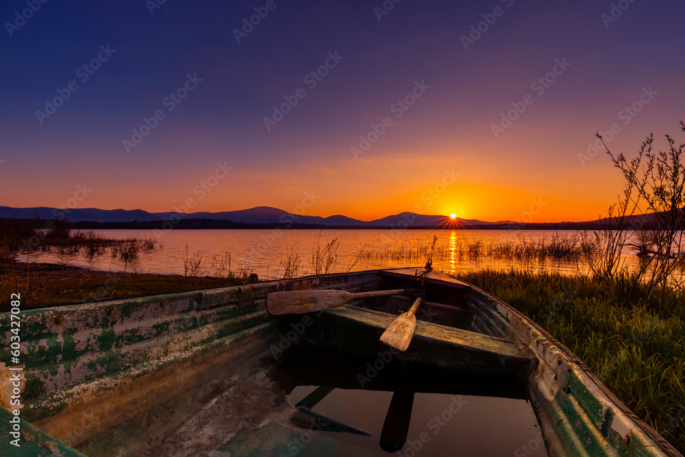 Malowniczy zachód słońca nad jeziorem ze starą łodzią z wiosłami i bezchmurnym niebem w tle, Polska - obrazy, fototapety, plakaty 