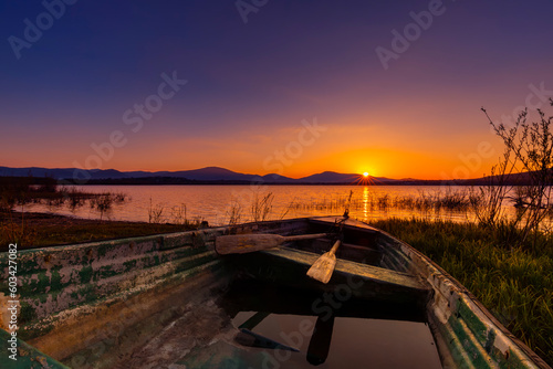Krajobraz wodny. Malowniczy zachód słońca nad jeziorem ze starą łodzią. Bezchmurne niebo w tle, Polska