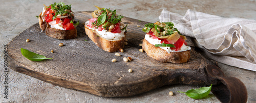 bruschettas with cream cheese, tomatoes and artichokes on a wooden board