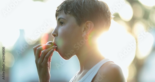 Young boy eating fruit outside during sunset lens-flare. Child eats healthy snack