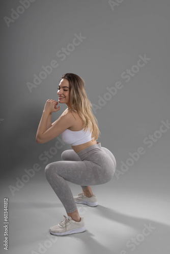 Squat exercises. attractive young fitness girl doing squat exercises in studio with gray background and smiling contentedly