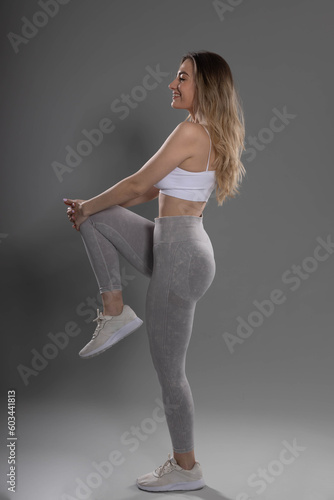 attractive young fitness girl doing leg stretching exercise in studio with gray background