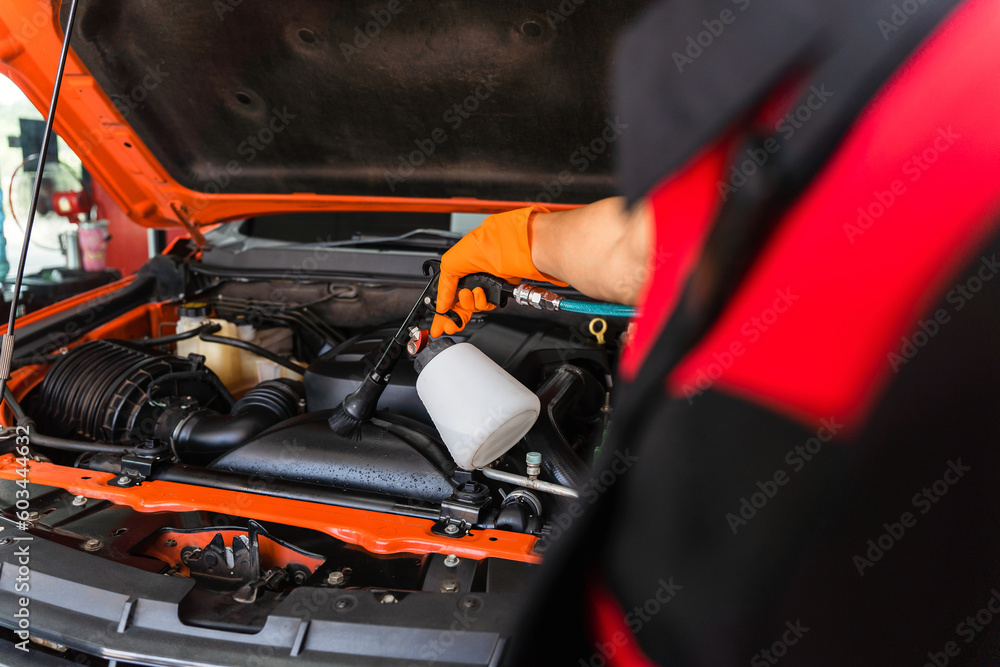 Asian young male employee using engine cleaning tool, employee cleaning engine, car washing, engine compartment cleaning.