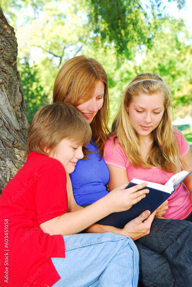 Portrait of a family - mother and children - reading a book in a park Portrait of a family - mother and children - reading a book in a park
