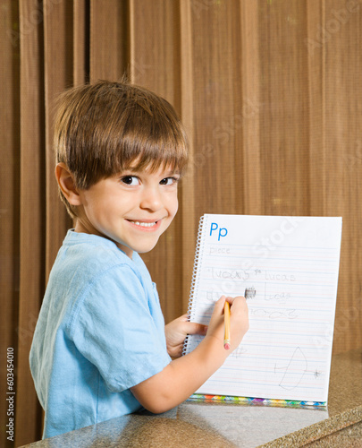 Hispanic boy holding up homework and smiling at viewer.