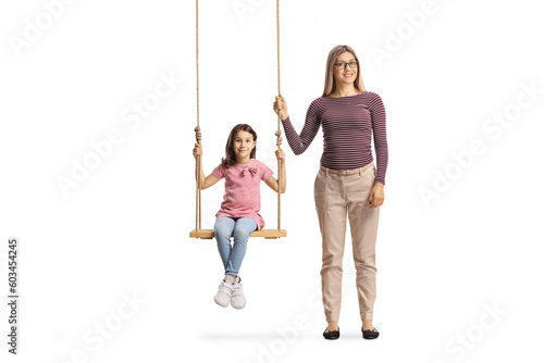 Full length portrait of a woman standing next to girl on a wooden swing