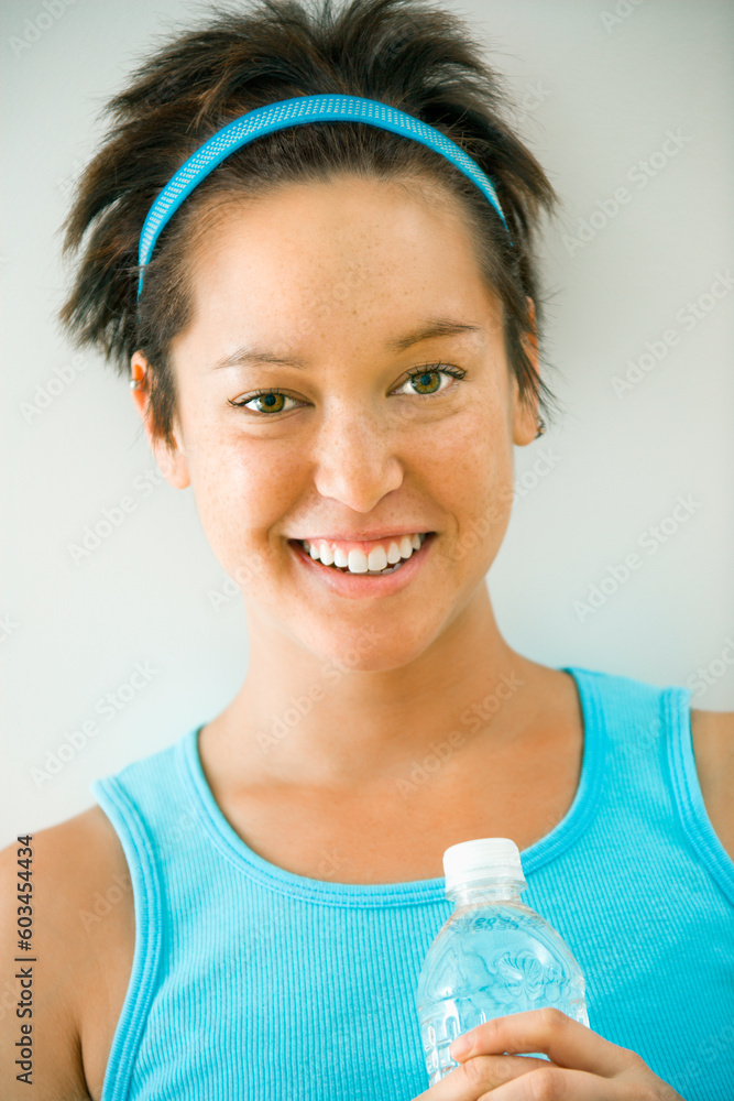 Head and shoulder portrait of young woman in fitness wear holding bottled water and smiling. Head and shoulder portrait of young woman in fitness wear holding bottled water and smiling.