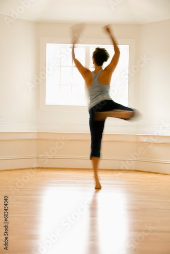 Young woman in motion jumping and dancing indoors by sunlit window.
