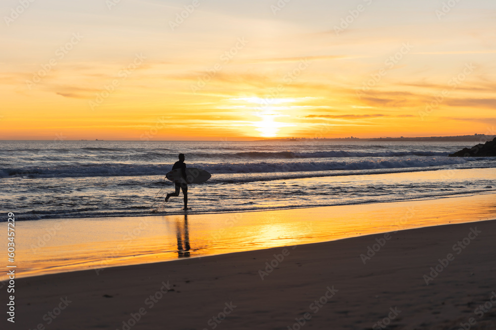 A man surfer running on the seashore at sunset