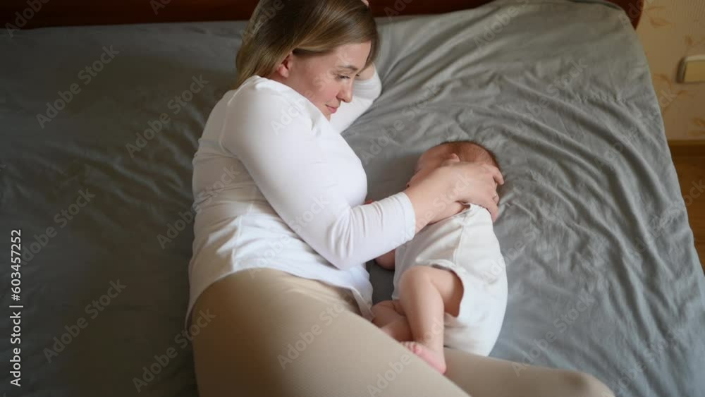 A beautiful mother lies on the bed next to a sleeping baby,strokes him,hugging. Child safety and protection, co-sleeping A beautiful mother lies on the bed next to a sleeping baby,strokes him,hugging. Child safety and protection, co-sleeping