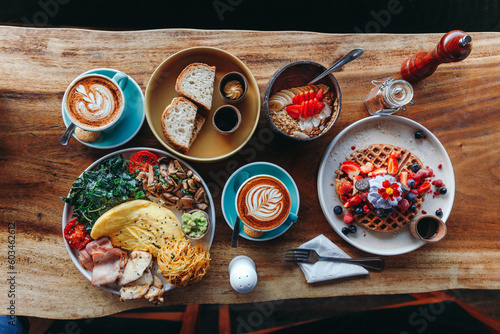 Morning breakfast on a table above, waffles with cream, berries, coffee, cappuccino, bowl, omlet with vegetables, bread with butter, avocado cream, vegan food, healthy food, meal.