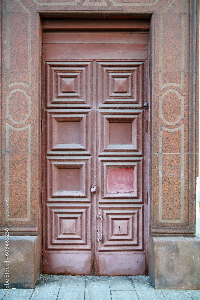 A tall old wooden door with a square ornament is closed with a padlock