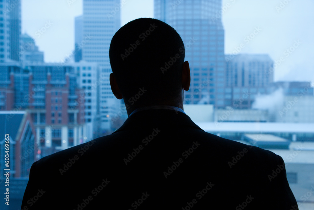 Rear view of an African-American businessman looking out of a window at the city in the distance. Horizontal shot.