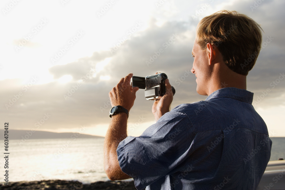 Obraz premium Smiling Caucasian man photographing a scenic sunset at a beach. Horizontal format.