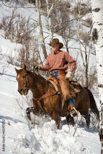 Cowboy in chaps riding a horse in the snow. Vertical shot.