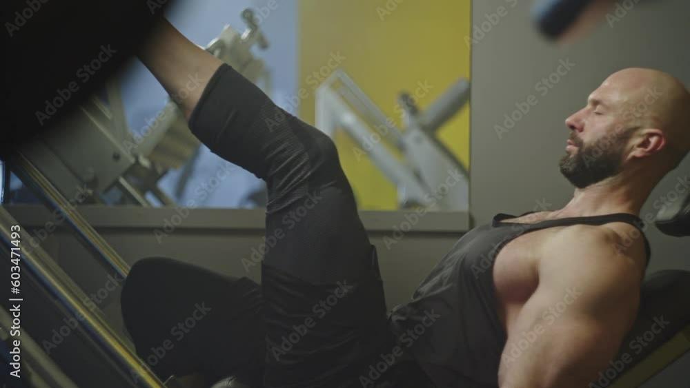 Male athlete trains his legs on the exercise machine in the gym. Caucasian bodybuilder doing workout and fitness. High quality 4k footage Male athlete trains his legs on the exercise machine in the gym. Caucasian bodybuilder doing workout and fitness. High quality 4k footage