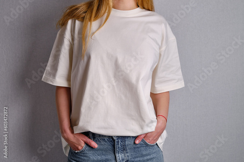Woman in a white T-shirt poses near a white wall. Hand gestures and emotions. Studio photography. The concept of emotion, strength and fun. Casual wear. Space for inscriptions and logo 