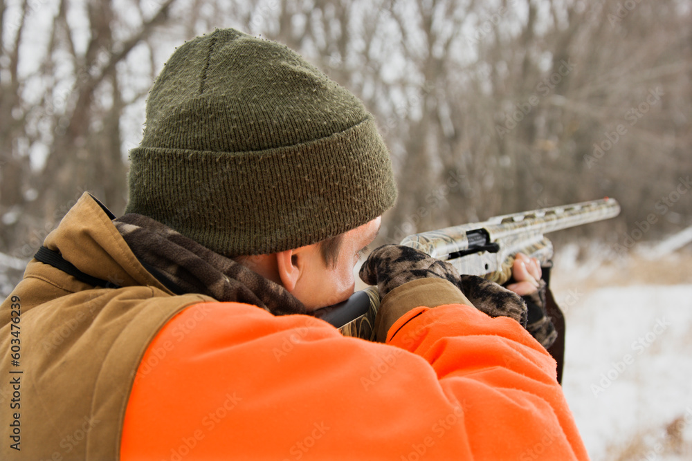 Caucasian male aiming shotgun out towards woods. Caucasian male aiming shotgun out towards woods.