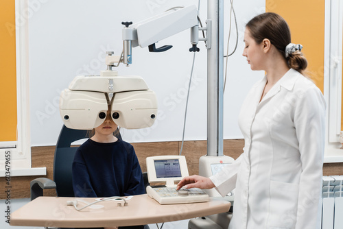 Child looks into phoropter during an eye examination of pediatric ophthalmologist. Phoropter for measuring refractive error and determining information for prescription for eyeglasses.