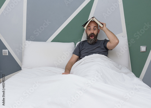 Bearded man reading a book in bed