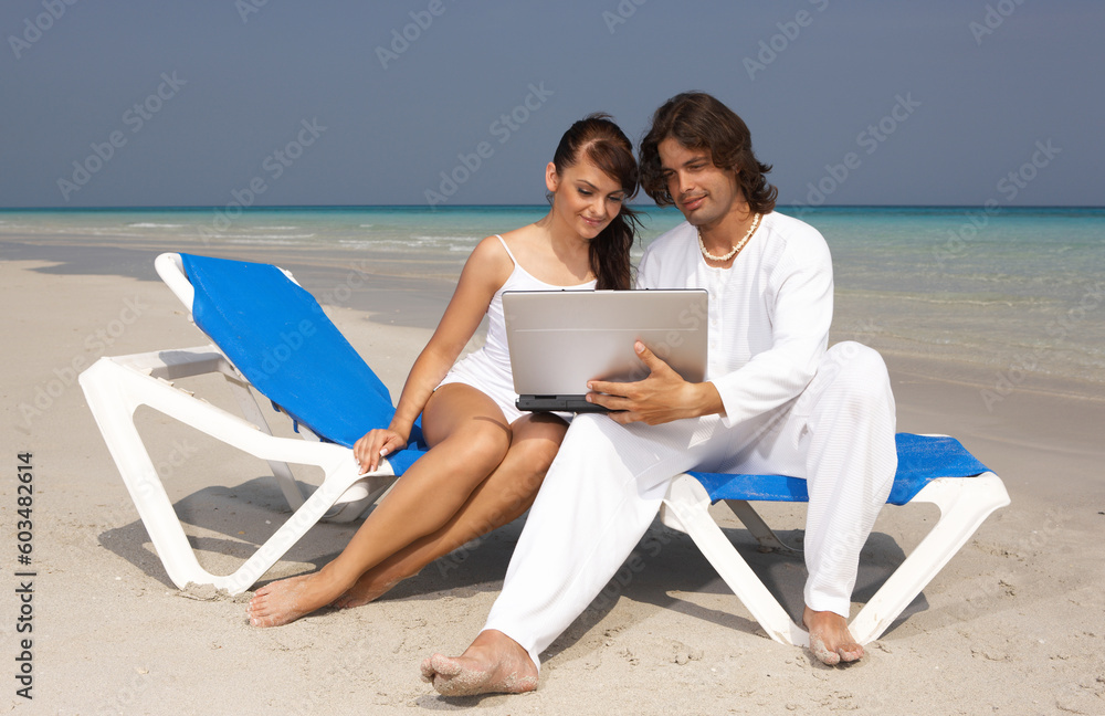 Romantic young couple working on laptop computer at the beach