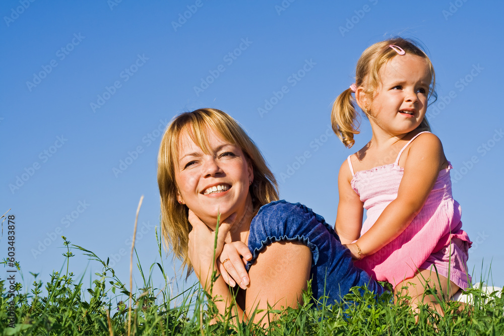 Woman and little girl laying in the grass against sunny summer sky Woman and little girl laying in the grass against sunny summer sky