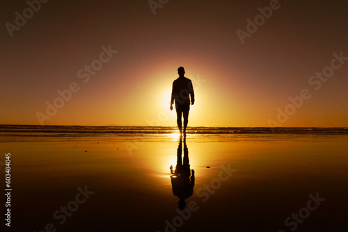 Photos Silhouette of a young man walking on the beach backlit by setting sun and his re