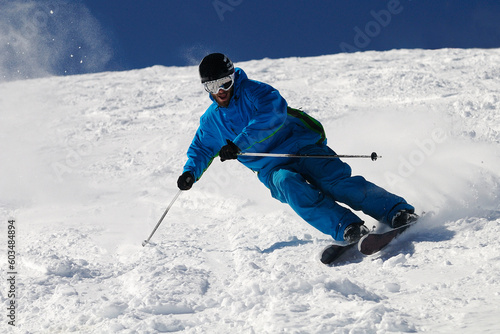 Schilderij op canvas Skier moving down on ski slope against blue sky.