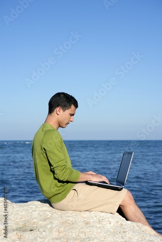 Handsome young businessman with computer on the blue ocean beach