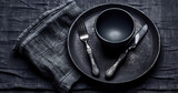 An empty black plate with cutlery on a dark concrete background. Home dinner cooking on stone table. Top view with copy space