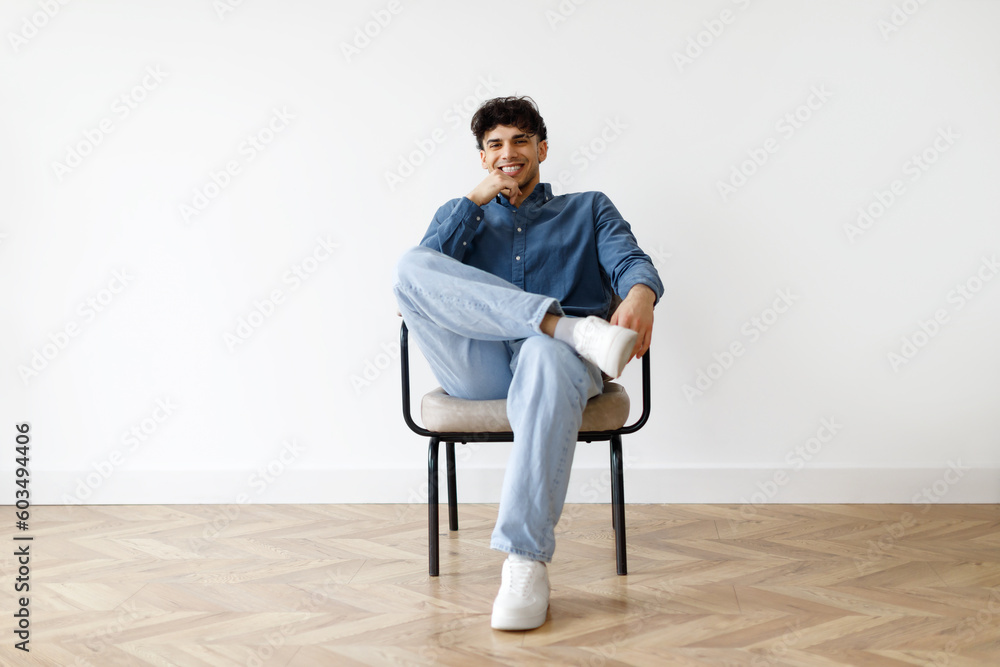 Happy arabic man relaxing sitting in armchair against white wall