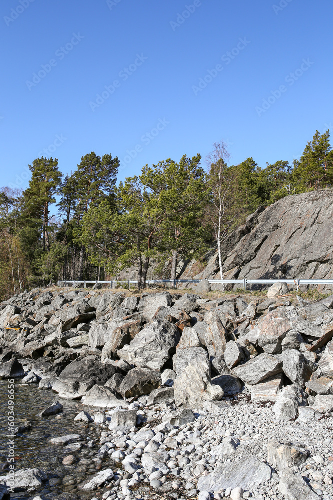 Cliff road metal barrier view scene with many rocks and clear blue sky.