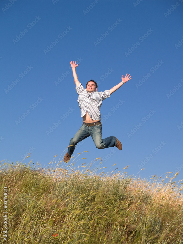 Happy jumping male teenager above green grass hill Happy jumping male teenager above green grass hill