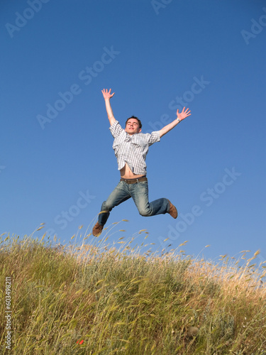 Happy jumping male teenager above green grass hill