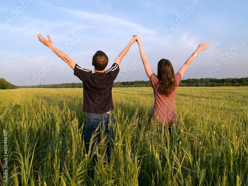 Young Couple in Field Holding Hands Up Rear View
