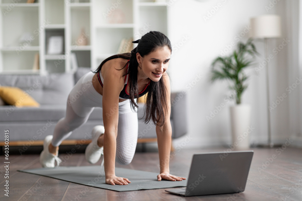 Obraz premium Beautiful athletic young woman have workout at home, using laptop
