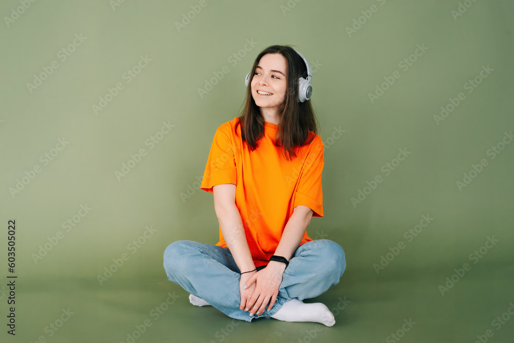 Portrait of a dreamy woman with headphones looking into the distance, isolated on a vibrant green background. Portrait of a dreamy woman with headphones looking into the distance, isolated on a vibrant green background.