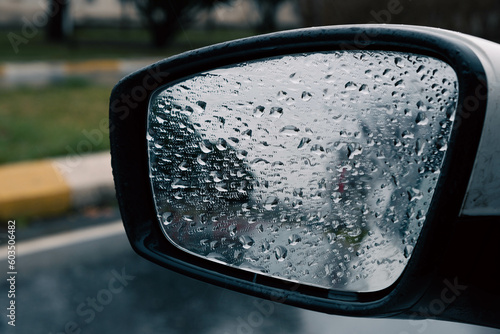 Raindrops cover the car mirror on a rainy day, obscuring the view with an abundance of droplets, creating a hazy and obscured reflection.