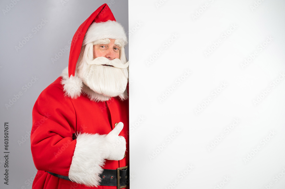 Santa claus peeks out from behind an empty Christmas advertisement and shows a thumbs up. Santa claus peeks out from behind an empty Christmas advertisement and shows a thumbs up.