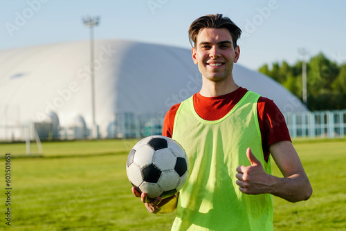 Young smiling man football player holding soccer ball with thumb up, copy space