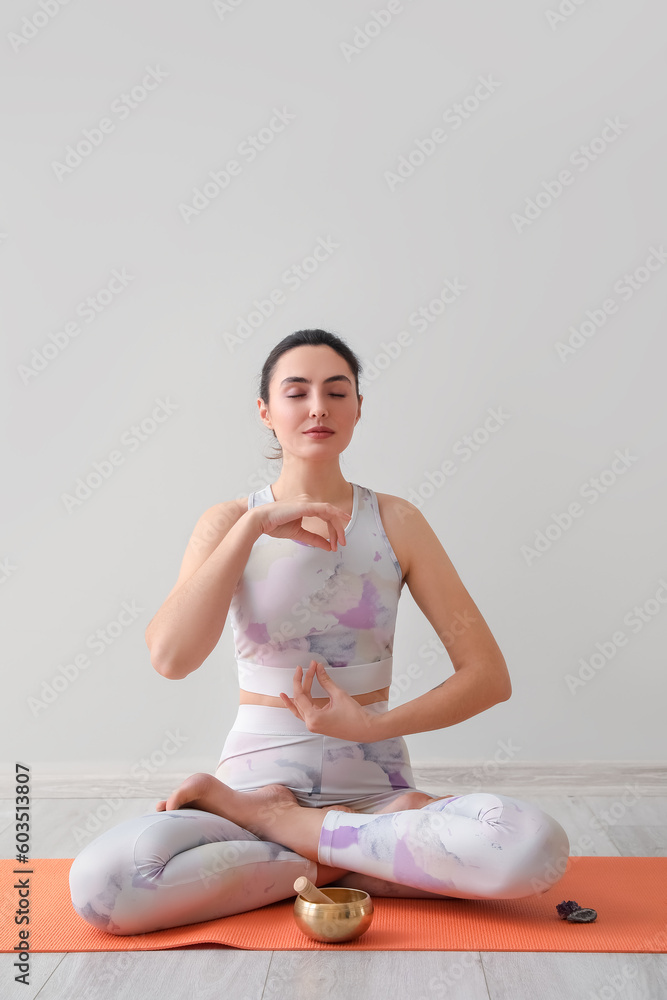 Beautiful meditating young woman with Tibetan singing bowl at home