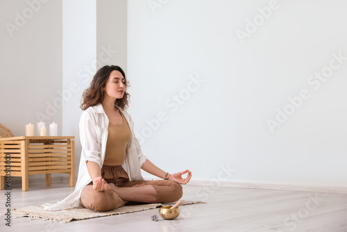 Beautiful meditating young woman with Tibetan singing bowl at home
