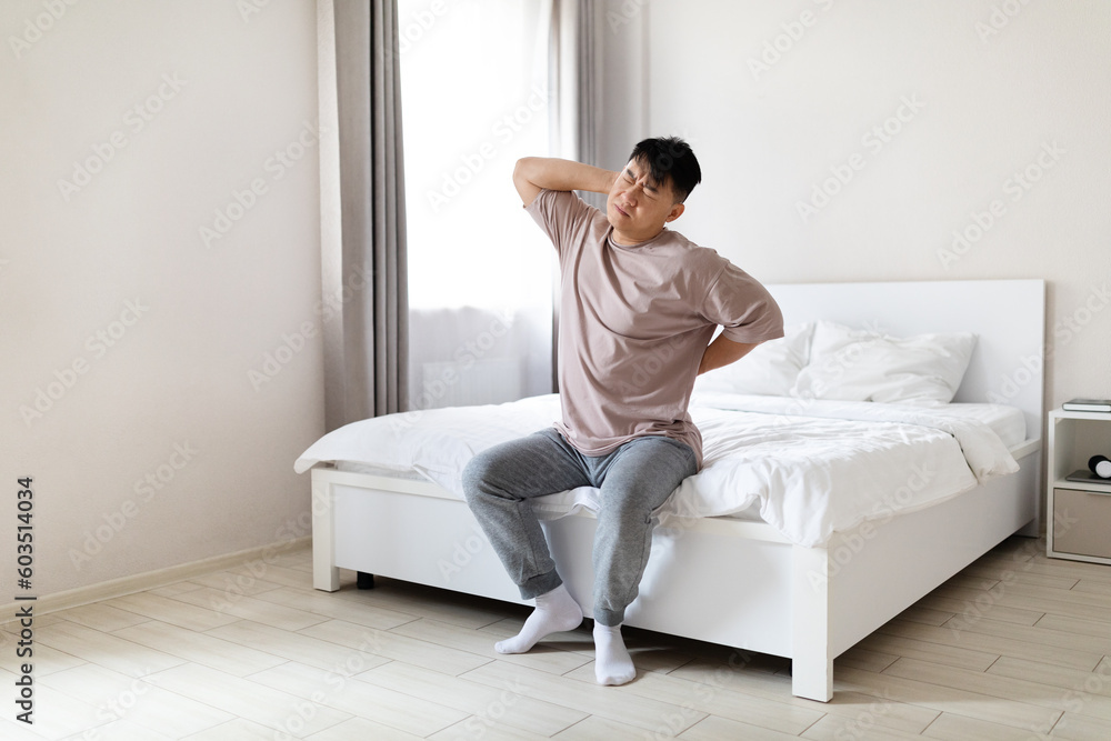 Tired asian man suffering from back pain after waking up Tired asian man suffering from back pain after waking up