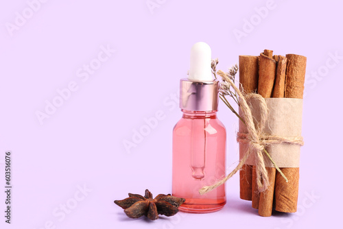 Bottle of essential oil, cinnamon sticks and anise star on color background