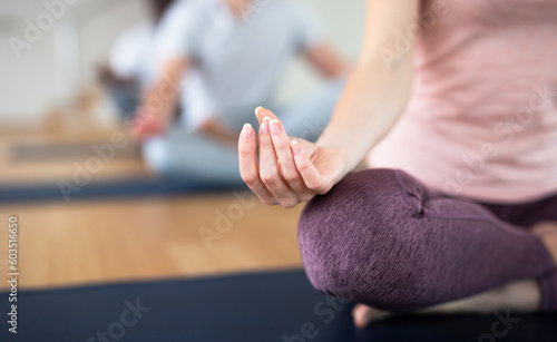 Young woman meditating in lotus position with hands folded in mudra on her knees during group yoga class, cropped shot..