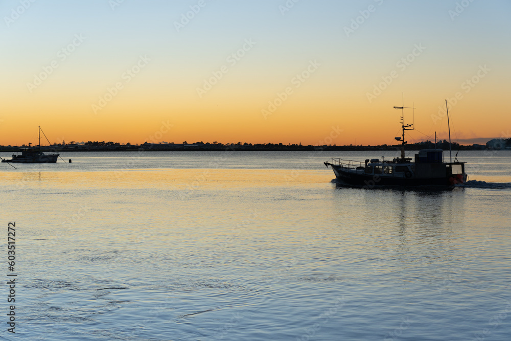 Commercial fishing boat leaving in morning light in silhouette